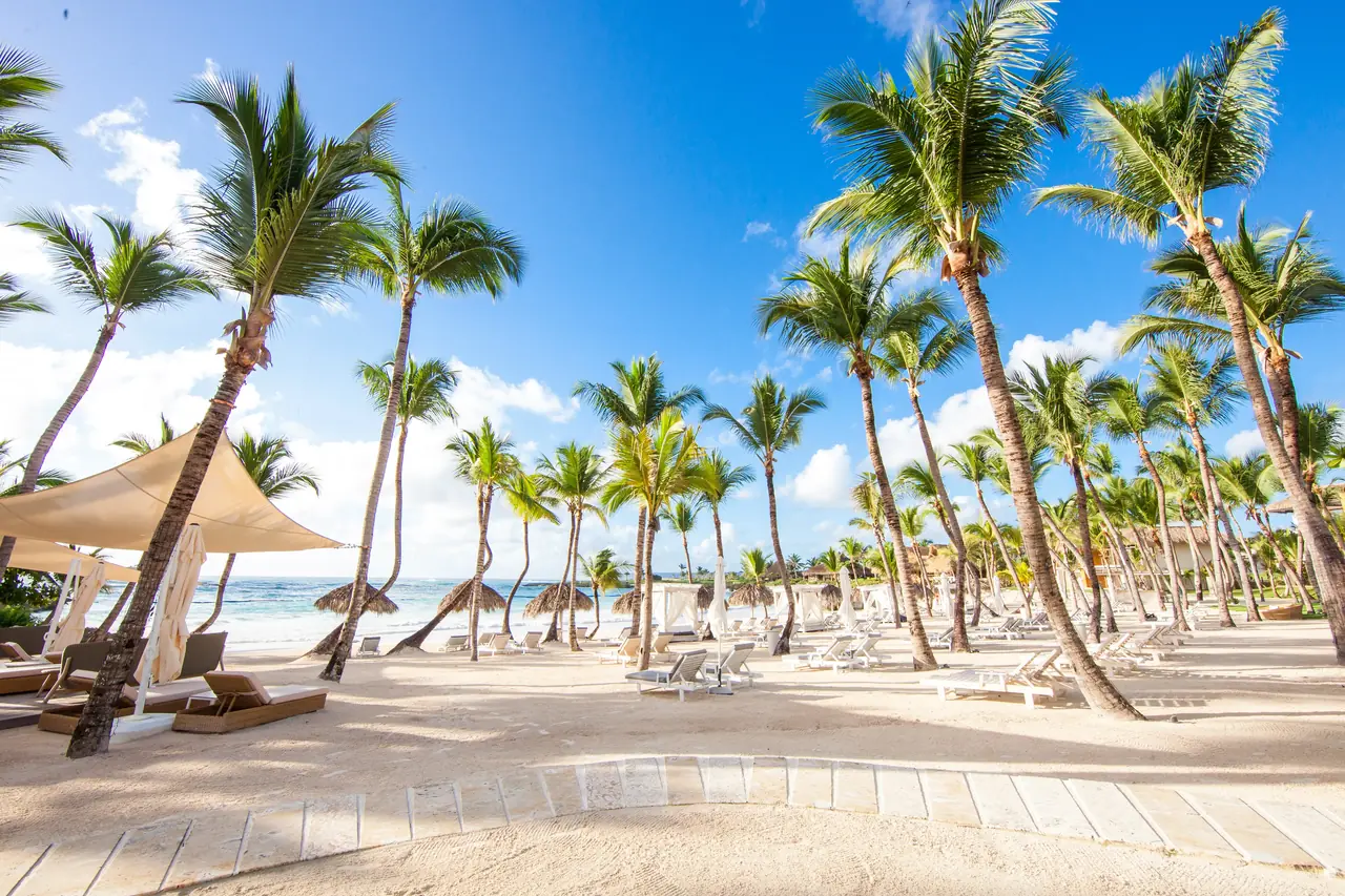 Palm-lined white-sand beach with sun loungers and cabanas at Eden Roc Beach Club, Cap Cana